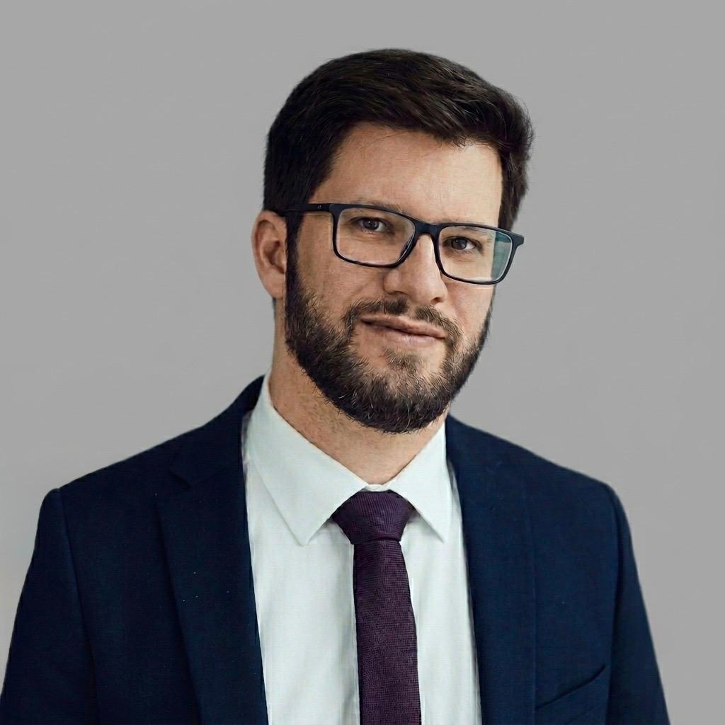 Professioneller Mann mit Brille und dunklem Anzug vor grauem Hintergrund, geeignet für Rechtsanwalt im Erbrecht